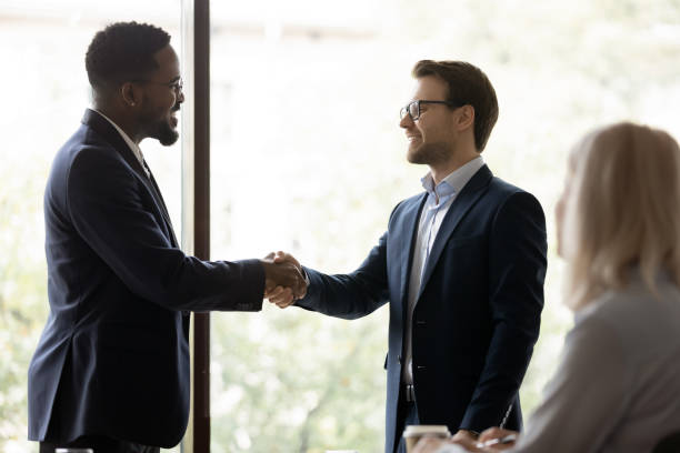istock Happy male colleagues shake hands in office 1276706763