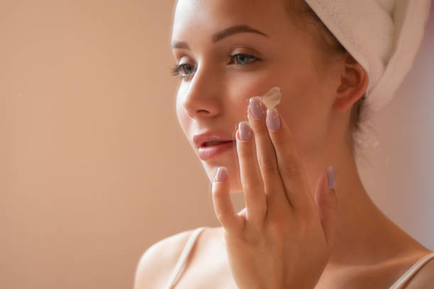 istock Young attractive woman applying cream to her face while looking at her reflection in the mirror. Beauty photography 1276709530