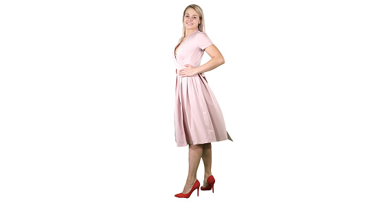 Full length portrait. Woman in a pink dress making a turn and looks at her self like in the mirror on white background. Professional shot in 4K resolution. 005. You can use it e.g. in your commercial video, business, presentation, broadcast