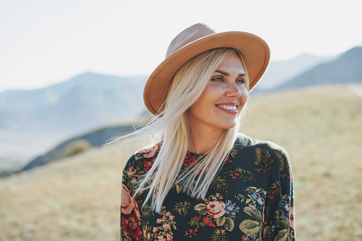 Beautiful smiling blone young woman traveler in dress and felt hat on road, trip to mountains, Altai