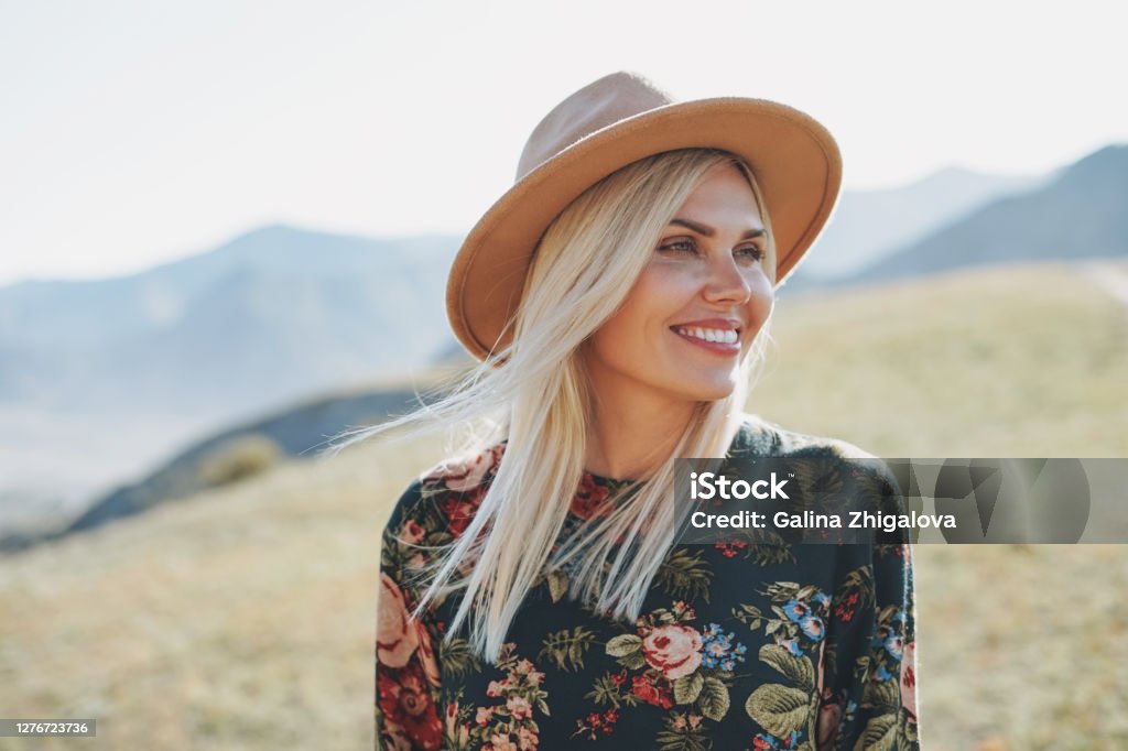 Beautiful smiling blone young woman traveler in dress and felt hat on road, trip to the mountains, Altai Beautiful smiling blone young woman traveler in dress and felt hat on road, trip to mountains, Altai Women Stock Photo