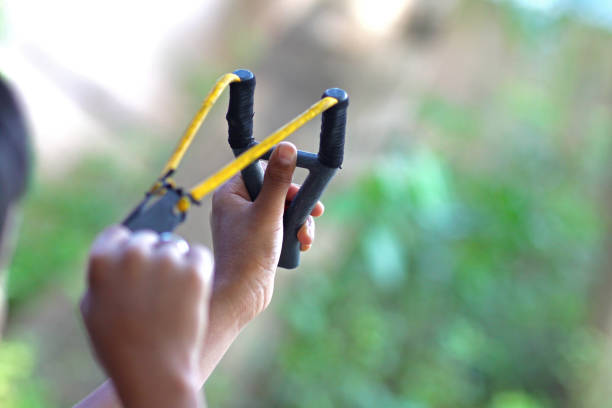 close up, wide angle shot of a 11 years old  boy aiming with a classic slingshot, focus in left hand