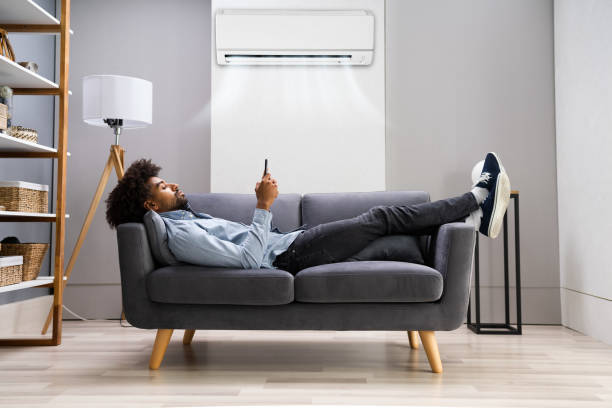 istock Young Man Lying Under Air Conditioner On Couch Using Smartphone 1276732842