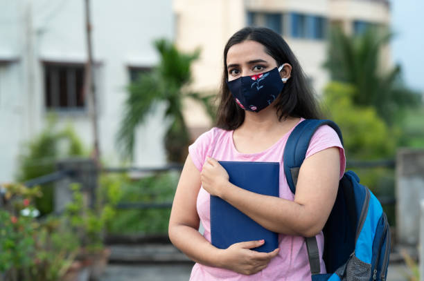 College or university student wearing protective face mask in a campus College or university student wearing protective face mask in campus and holding Laptop or books. Young Student wearing protective face mask and standing near School or College building , Back to school after COVID-19 pandemic. Horizontal composition with extra copy space. teenage girls pretty smile looking at camera waist up stock pictures, royalty-free photos & images