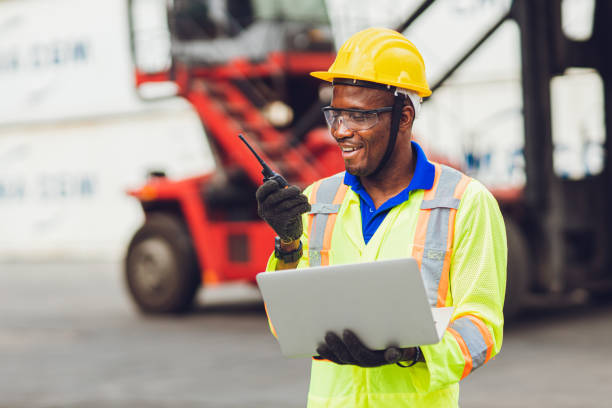 istock African American black worker working in logistic shipping cargo port site happy work control loading with radio and laptop. 1276735622