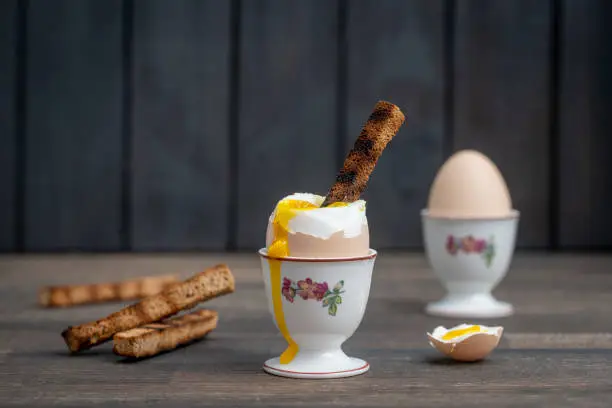 Soft boiled brown egg and toast bread in eggcup on wooden table background. Close up. Healthy breakfast