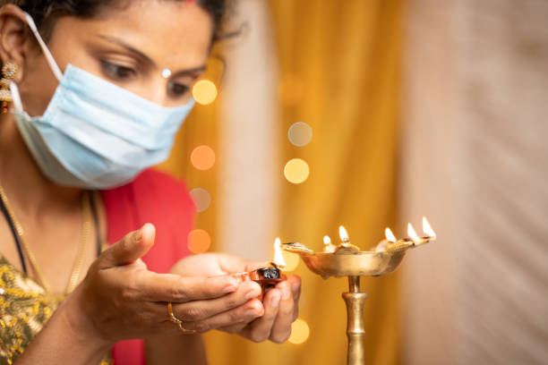 手に選択的に焦点を当てる,自宅での祭りの間に医療マスク照明ランタンまたはディヤランプのインドの女性 - コロナウイルスまたはcovid-19パンデミックの間に伝統的な祭りのお祝いの概念 - india palace indian culture indoors ストックフォトと画像