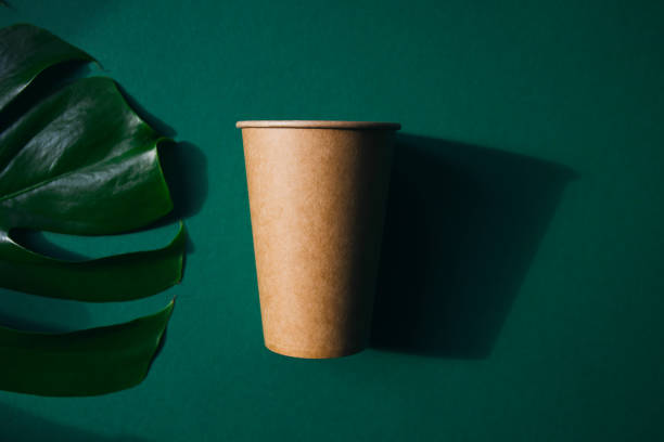 istock Eco friendly craft paper cup on green background with monstera leaf. 1276741495