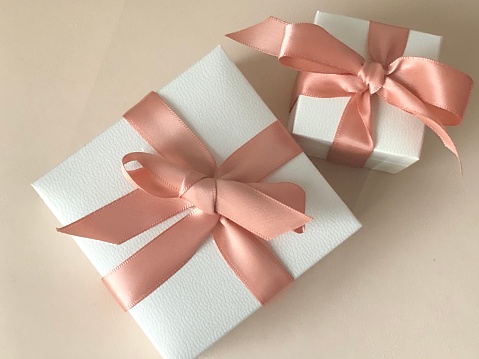 Mother's Day concept. Gift box with golden ribbons on a pastel powder background with empty space for text.
