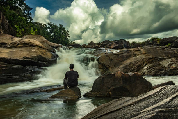 istock man sitting at a rock watching the beautiful waterfall stream at evening 1276743579