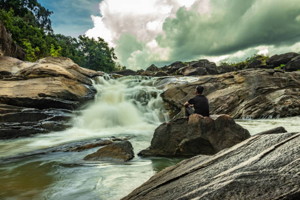 istock man sitting at a rock watching the beautiful waterfall stream at evening 1276743639