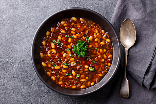 Bean soup in a black bowl. Grey background. Close up. Top view.