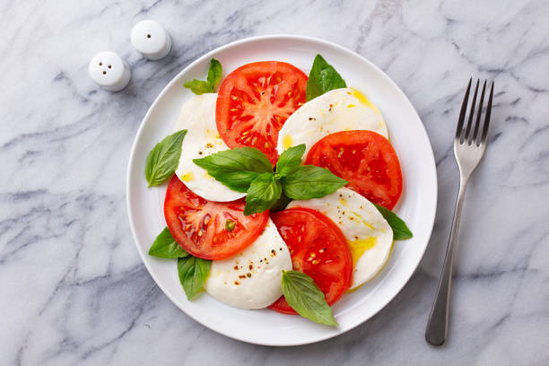 Caprese salad with tomatoes, mozzarella cheese and basil on a white plate. Marble background. Close up. Top view. stock photo