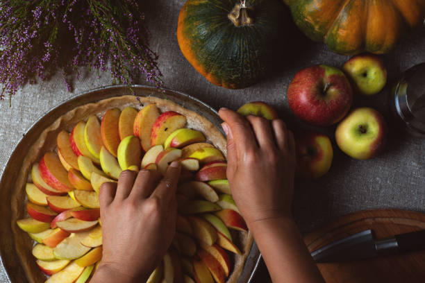istock Preparation, Thanksgiving Day celebration. The chef finishes adding apples to the pie. Making a traditional apple pie. Nearby are yellow-green pumpkins. 1276753958
