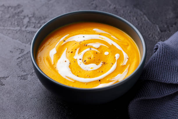 istock Pumpkin soup with cream in black bowl. Dark grey background. Close up. 1276754095