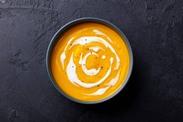 Butternut squash soup with cream in black bowl. Dark background. Top view.