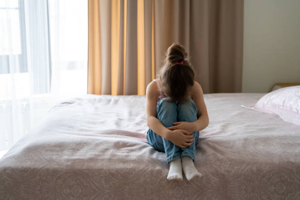 istock A little sad girl sitting on a bed, back view 1276763839