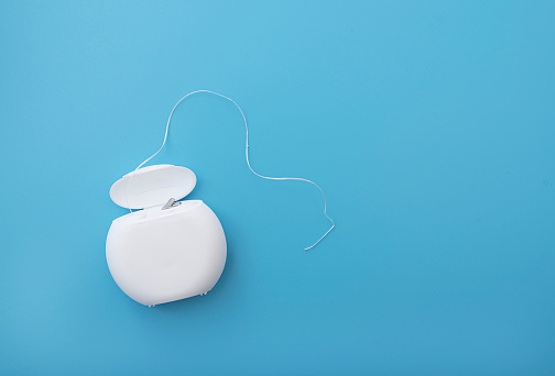 Dental floss in white plastic container on blue surface with space for text, top view, concept picture about medicine