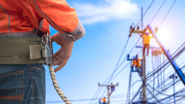 Midsection of electrician lineman wearing safety belt with blurred background of electrical workers team are working on power poles in public area Midsection of electrician lineman wearing safety belt with blurred background of electrical workers team are working on power poles in public area pole photos stock pictures, royalty-free photos & images