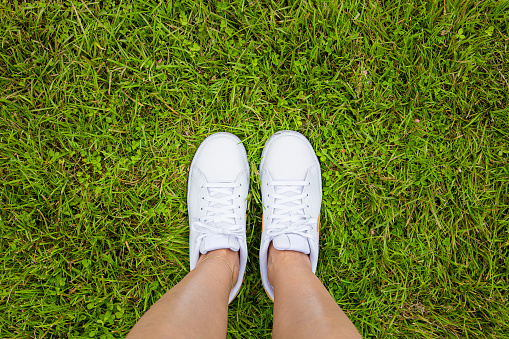Young woman standing in lawn, top view of casually dressed youth person in white sneakers over grassy field