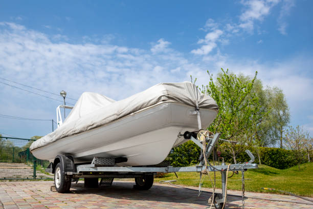 istock Big modern inflatable motorboat ship covered with grey or white protection tarp standing on steel semi trailer at home backyard on bright sunny day with blue sky on background. Boat vessel storage 1276775158