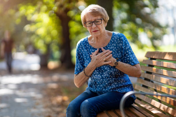 Senior Woman Suffering From Chest Pain While Sitting On Bench Senior Woman Suffering From Chest Pain While Sitting On Bench senior adult women park bench 70s stock pictures, royalty-free photos & images