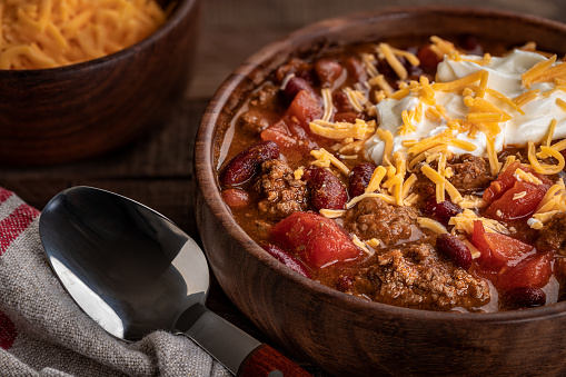 Closeup of bowl of chili con carne with shredded cheddar cheese and sour cream
