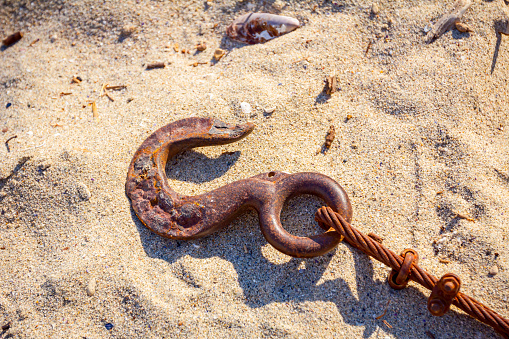 Aged rusty anchor with strong rope is placed on the sandy beach.