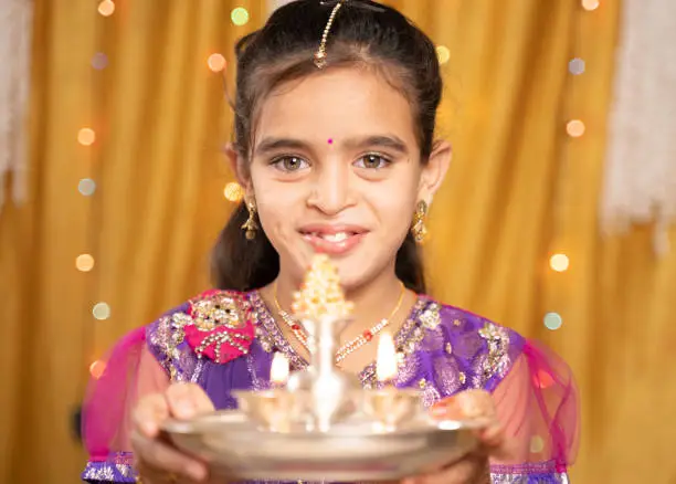 POV shot of cute little girl in traditional dress doing aarti or offering light to god during Hindu Religious festival ceremony