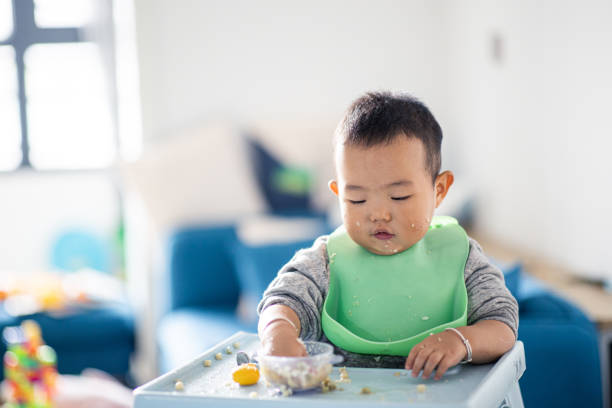 Baby child eating self sitting in chair