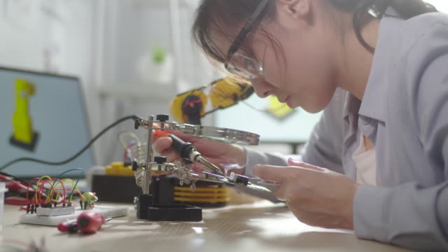 Female Engineer girl repairing the circuit board with soldering iron and wire