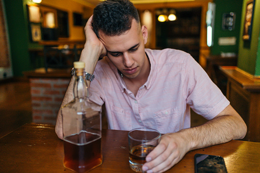 Young depressed man addicted to alcohol drinking whiskey alone in bar