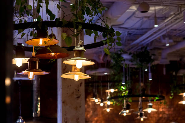 istock retro lanterns with round lamps and edison lamp with warm glow are suspended from ceiling with green leaves of eco friendly cafe, decorative light in interior of night restaurant, nobody. 1276796371