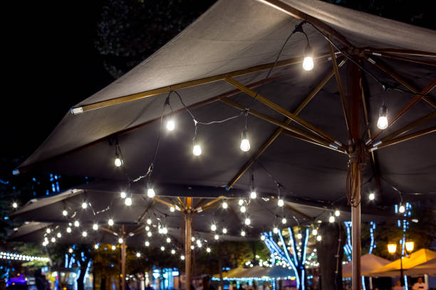 istock textile umbrella with a wooden frame and edison pendant lamps glowing with light on a backyard terrace night scene, nobody. 1276796374