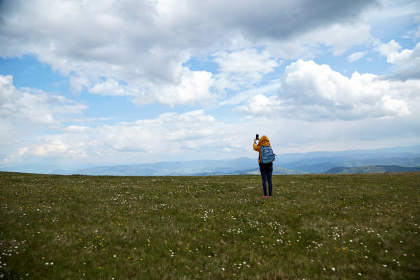 istock One woman using cellphone on a big meadow and landscape mountain top view. 1276797126