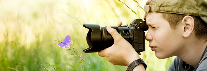 Photographer teenager shooting butterfly on the wild flower on nature in summer day