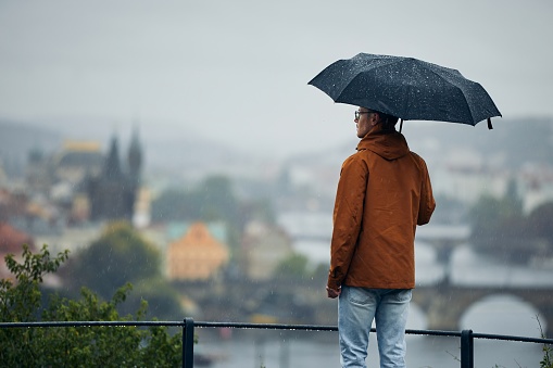 Young man with umbrella looking at city in the heavy rain. Gloomy day in Prague, Czech Republic