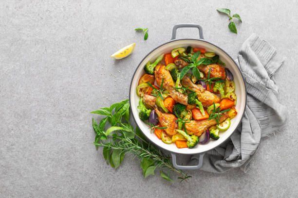 Chicken drumsticks roasted with vegetables in cast iron pan on kitchen table, top down view