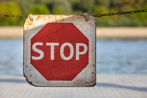 Stop sign on suspended chain. Road sign to warn to stop. Background with nature and vegetation.