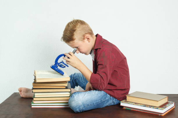 istock A schoolboy sits at a table near books and looks through a microscope. 1276819369