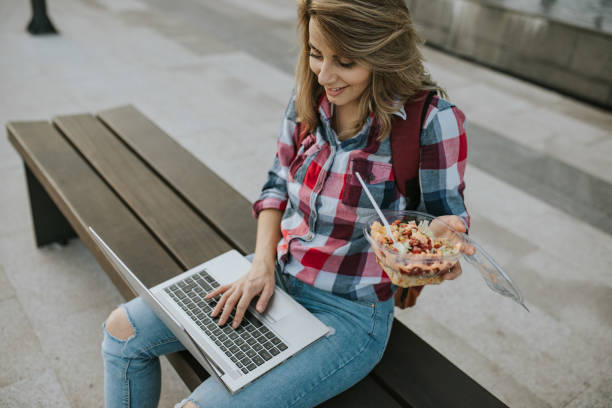istock Female student eating and using her laptop in front of college 1276822850