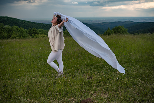 Woman is holding fabric on wind in nature