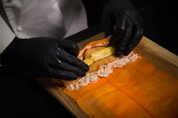 istock Chef wrapping Japanese no rice sushi roll into carrot daikon. Rolling sushi without rice in black protective gloves 1276830715