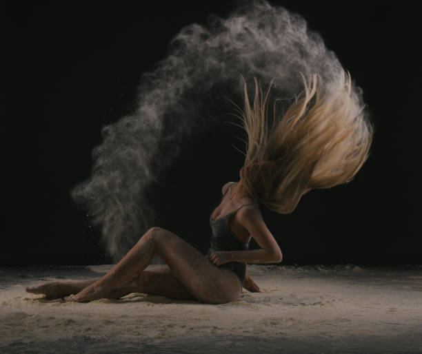 istock Dancer with long blond hair throwing dust, flour, powder on black background. 1276831645