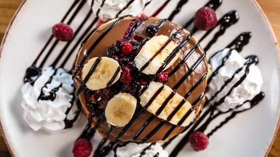 Delicious pancakes topped with chocolate sauce, banana slices and berries