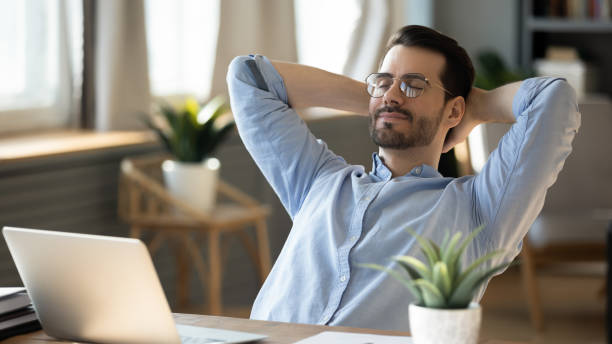 Calm young man relax in chair at home workplace Calm millennial man in glasses sit relax at home office workplace take nap or daydream. Happy relaxed Caucasian young male rest in chair distracted from computer work, relieve negative emotions. inhaling stock pictures, royalty-free photos & images