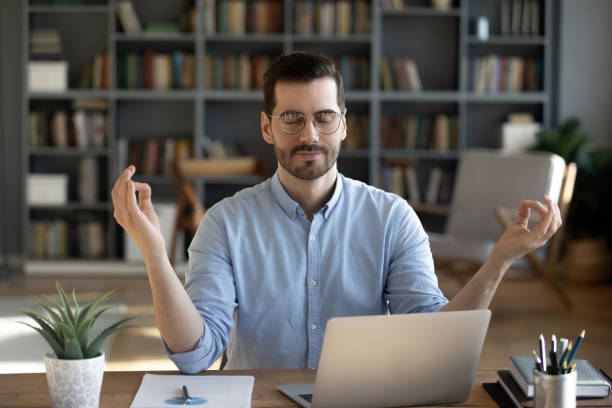 Calm Caucasian male worker meditate at workplace Calm young Caucasian male employee sit at home office workplace practice yoga relieve negative emotions. Relaxed mindful man meditate with mudra hands with eyes closed. Stress free, balance concept. meditation room office stock pictures, royalty-free photos & images