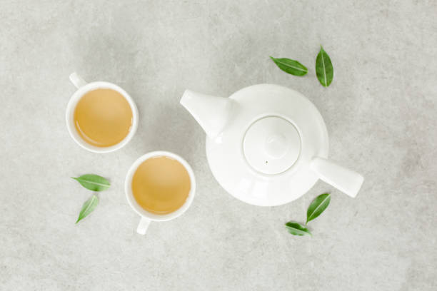 istock Herbal tea with two white tea cups and teapot, with green tea leaves. Flat lay, top view. Tea concept 1276839676