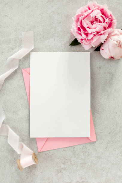 istock Mockup invitation, blank paper greeting card, pink envelope and peonies on gray stone table. Flower background. Flat lay, top view 1276839733