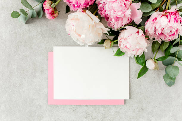 istock Mockup invitation, blank paper greeting card, pink envelope and peonies on gray stone table. Flower background. Flat lay, top view 1276839910